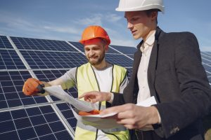 Engineer and businessman in hard hats discussing a solar energy project during a customer consultation.